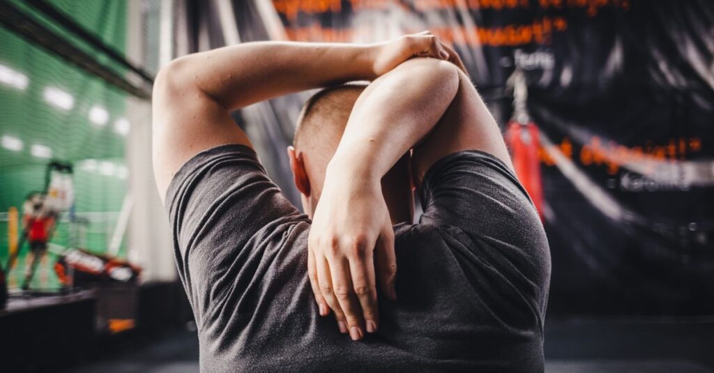 Man stretching arms in a gym, viewed from behind, focusing on fitness and flexibility.