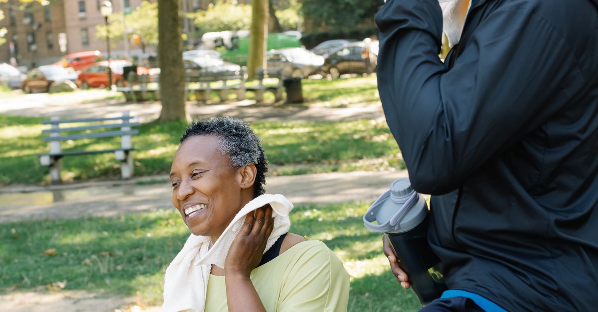 Two adults cooling down with towels after an outdoor workout in a sunny green park.