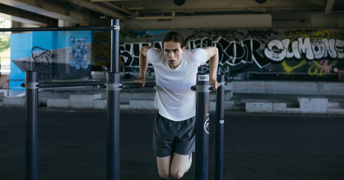 Athletic man in urban setting exercises on bars with vibrant graffiti background, showcasing flexibility.