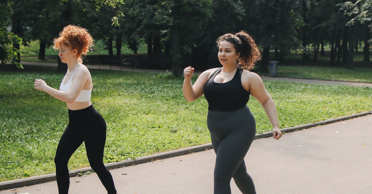 Two women power walking on a park path, enjoying outdoor fitness.