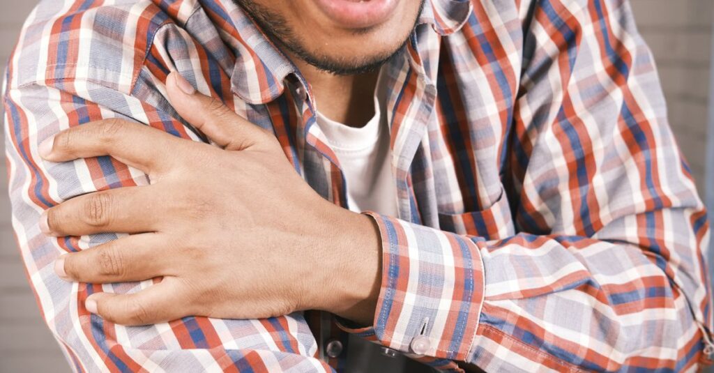 Close-up of a man in plaid shirt experiencing shoulder pain, grasping his arm.