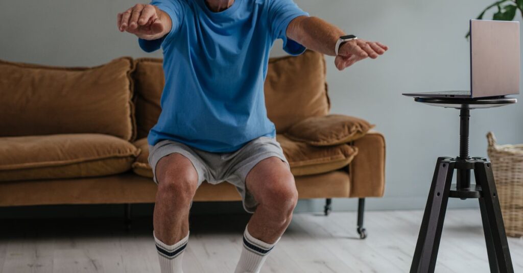 A senior man performing squats with dumbbells on a mat indoors for a healthy lifestyle.
