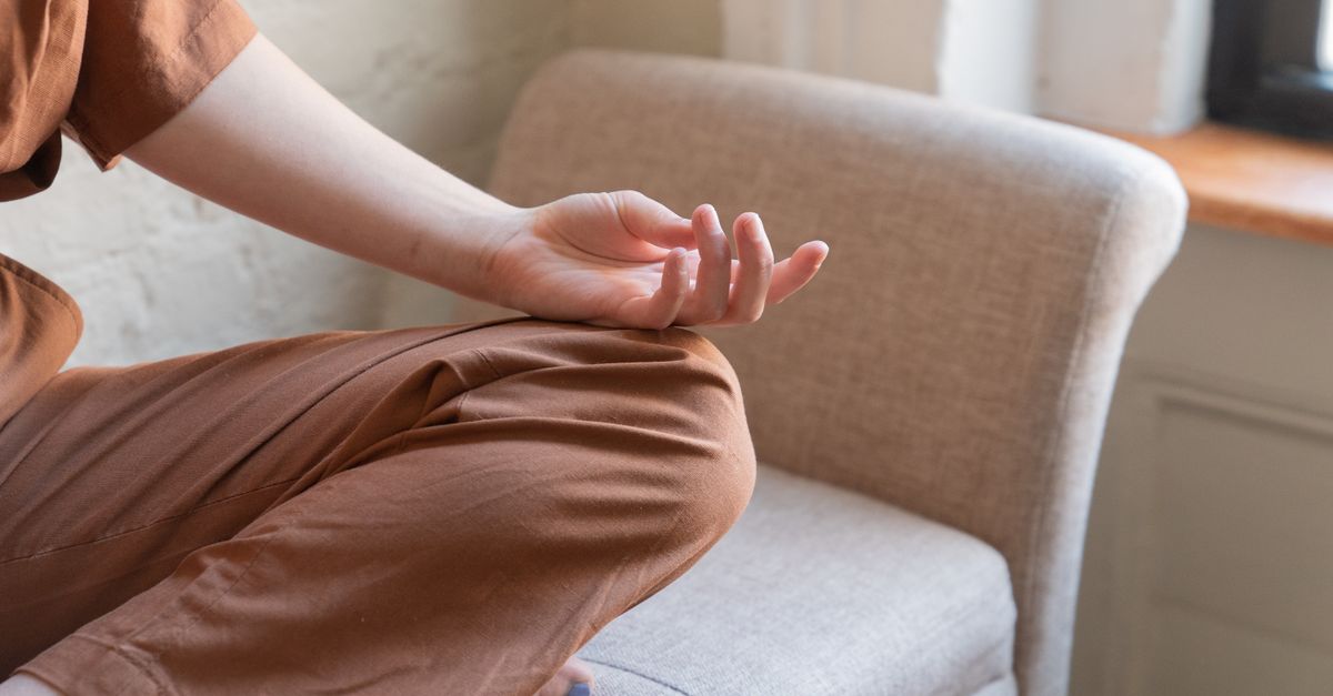 Close-up of a person meditating indoors on a comfortable armchair.