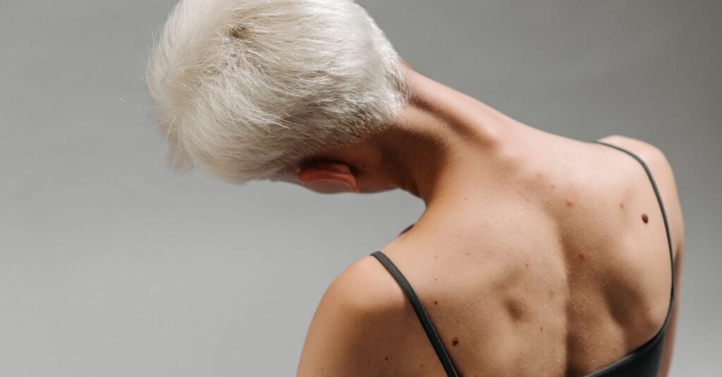 Back view of a woman with white hair bending her neck, showing body movement and detail on gray background.